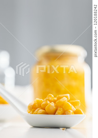 Canned sweet corn on ceramic spoon on white table. 120188242