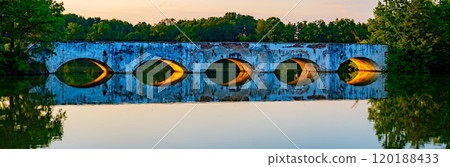 The historic stone bridge, built in the late 18th century, arches gracefully over Vitek Pond, reflecting the warm colors of evening light amidst serene natural surroundings. The historic stone bridge, built in the late 18th century, arches gracefully over Vitek Pond, reflecting the warm colors of evening light amidst serene natural surroundings. 120188433
