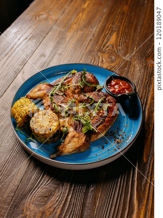 Grilled chicken with corn on the cob and a side of spicy dipping sauce on a blue plate 120189047