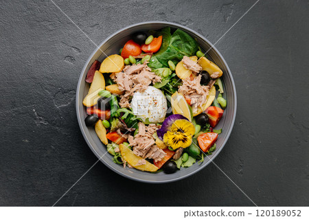 Gourmet salad bowl with tuna, poached egg, colorful vegetables, and edible flower garnish 120189052