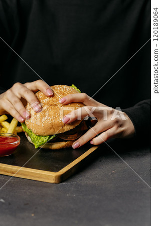 Close up of hands holding juicy burger with crispy fries and ketchup on the side Close up of hands holding juicy burger with crispy fries and ketchup on the side 120189064