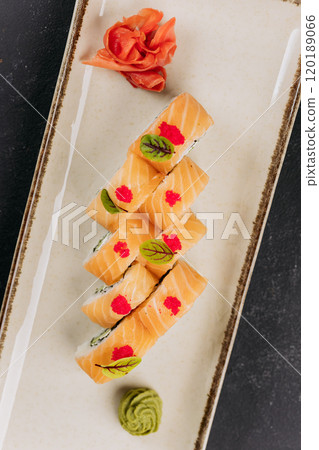Close-up of sushi rolls with salmon, cream cheese, and cucumber, garnished with wasabi and roe 120189066
