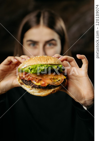 Excited woman holding a juicy burger with fresh toppings, capturing the joy of indulgent dining 120189074