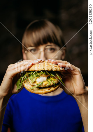 Woman holding a gourmet burger with fresh greens and cheese, ready to take a delicious bite 120189080