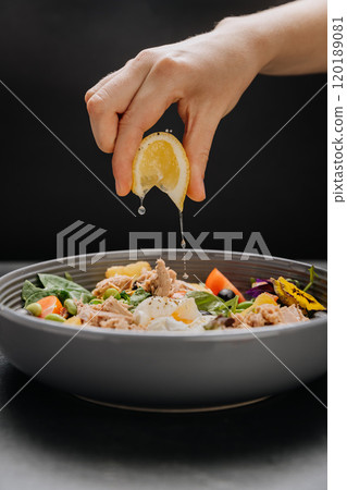 Fresh lemon juice squeezed over a nutritious tuna salad with poached egg, greens and vegetables 120189081