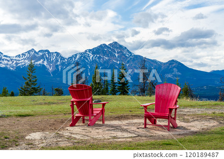 Red adirondack chairs on top of Old fort point trailhead. Jasper National Park nature scenery. Alberta, Canada. Forest and snow capped mountains in summer. Pyramid Mountain. Canadian Rockies. 120189487