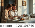 A young couple sits at a table, sharing a moment over breakfast with coffee and pastries while reading a newspaper. The warm sunlight filters through the window, creating a cozy atmosphere that 120189740