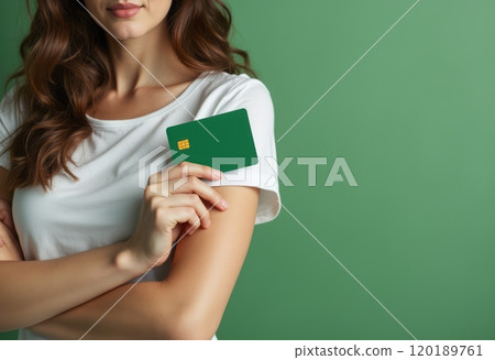 A young woman with wavy hair is holding a green credit card close to her chest against a solid green background. The image conveys a sense of financial empowerment and modern lifestyle, highlighting 120189761