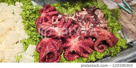 Fresh octopus arranged on a bed of lettuce at a seafood market. Vibrant colors highlight the octopus's texture, creating an enticing display for seafood enthusiasts 120190303