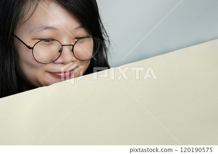 Portrait of a young Asian woman with black round glasses looking at an empty white light brown paper with a smile on her face. 120190575