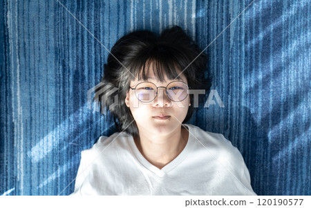 Cute short hair - glasses Asian woman laid on blue carpet. Cute short hair - glasses Asian woman laid on blue carpet. 120190577