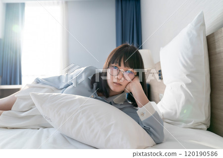 Asian young glasses woman lie on her side on the bed in the morning. 120190586