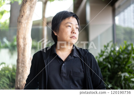 In a refined indoor environment, an Asian man in his middle age showcases his fashion prowess by wearing a sleek black polo shirt and a black cardigan in the indoor modern building. 120190736