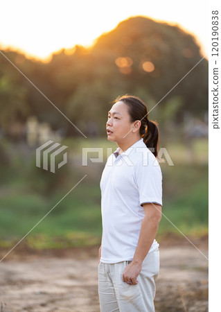 Asian Man long hair stands and relax on the dry field in golden twilight time. 120190838