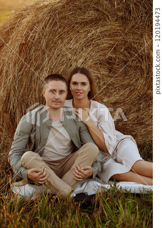 A couple is sitting on the grass next to a hay bale A couple is sitting on the grass next to a hay bale 120194473