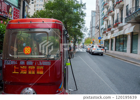 A red motorized rickshaw with Chinese characters and the number 88 stands out in a bustling Shanghai street, lined with modern buildings and greenery. A red motorized rickshaw with Chinese characters and the number 88 stands out in a bustling Shanghai street, lined with modern buildings and greenery. 120195639