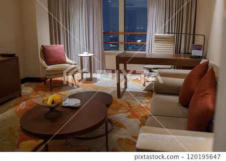 A modern hotel room in Shanghai features a seating area with a beige armchair, a wooden desk, and a large window offering a night view of the cityscape. A modern hotel room in Shanghai features a seating area with a beige armchair, a wooden desk, and a large window offering a night view of the cityscape. 120195647