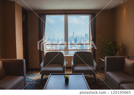 Cozy room with large window framing Shanghai skyline, featuring Oriental Pearl Tower. Furnished with chairs, table, and potted plant for a relaxing ambiance. Cozy room with large window framing Shanghai skyline, featuring Oriental Pearl Tower. Furnished with chairs, table, and potted plant for a relaxing ambiance. 120195665