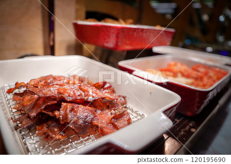 Crispy, glazed bacon strips are arranged in a white ceramic dish with a wire rack. Red ceramic dishes with other foods are visible in the background. Crispy, glazed bacon strips are arranged in a white ceramic dish with a wire rack. Red ceramic dishes with other foods are visible in the background. 120195690