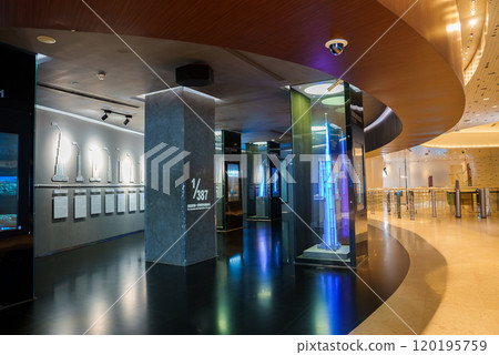 The exhibition space features modern design with polished floors and curved wooden ceilings. Scale models of skyscrapers are displayed, including a glass encased model. 120195759