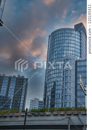 The image captures a modern Shanghai skyline with a cylindrical glass skyscraper reflecting the evening sky, surrounded by high rises and a rooftop garden. 120195811