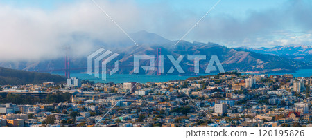 Aerial view of San Francisco with the Golden Gate Bridge in mist, dense urban cityscape, and Marin County hills in the background. 120195826