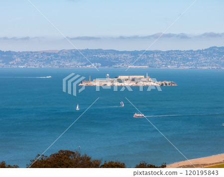 Alcatraz Island is surrounded by San Francisco Bay's blue waters, with boats and a sailboat. The cityscape and rolling hills form the backdrop. Alcatraz Island is surrounded by San Francisco Bay's blue waters, with boats and a sailboat. The cityscape and rolling hills form the backdrop. 120195843
