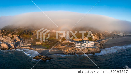 The iconic Cliff House stands above the Pacific Ocean, with waves crashing below and fog enveloping the hills in San Francisco, California. 120195867
