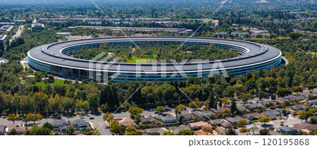 The image captures the circular Apple Park building, known as the spaceship, amidst greenery and suburban homes, showcasing its integration into the landscape. The image captures the circular Apple Park building, known as the spaceship, amidst greenery and suburban homes, showcasing its integration into the landscape. 120195868