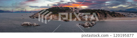 The image captures the San Francisco coastline with the Golden Gate Bridge, rocky shoreline, sandy beach, green hillside, and residential buildings. The image captures the San Francisco coastline with the Golden Gate Bridge, rocky shoreline, sandy beach, green hillside, and residential buildings. 120195877