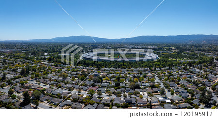 The image captures the circular Apple Park campus in Cupertino, California, surrounded by greenery and suburban homes, with the Santa Cruz Mountains in the background. 120195912