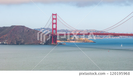 The Golden Gate Bridge spans the San Francisco Bay with its International Orange color. A sailboat navigates the blue waters, with Marin County hills visible. The Golden Gate Bridge spans the San Francisco Bay with its International Orange color. A sailboat navigates the blue waters, with Marin County hills visible. 120195968