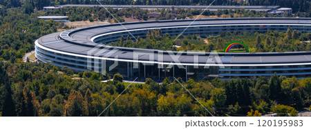 The image captures an aerial view of Apple Park in Cupertino, California, featuring its circular design, solar panels, and a rainbow arch in the courtyard. 120195983