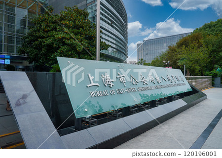 The image shows the Bureau of Exit Entry Administration in Shanghai, China, featuring a glass and steel building, lush greenery, and a clear blue sky. 120196001