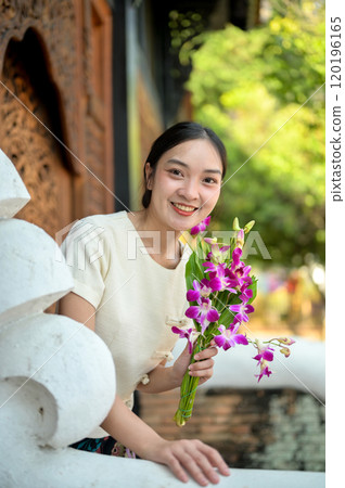 A charming Asian woman in a traditional dress stands by the temple, smiling at the camera A charming Asian woman in a traditional dress stands by the temple, smiling at the camera 120196165
