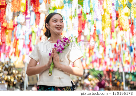 A smiling Asian woman stands in a temple with colorful lanterns in the background. 120196178