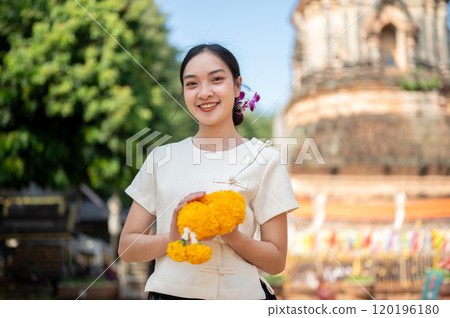 A charming Asian woman in a traditional Thai Lanna dress stands outdoors in a temple. 120196180