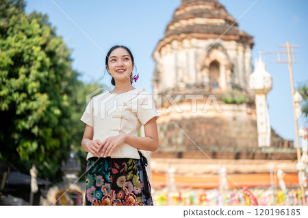A charming Asian woman in a traditional Thai Lanna dress with a temple in the background. A charming Asian woman in a traditional Thai Lanna dress with a temple in the background. 120196185