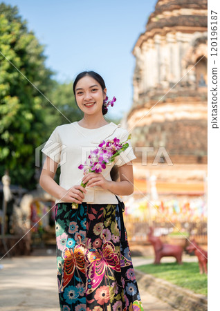 A charming Asian woman in a traditional Thai Lanna dress with a temple in the background. A charming Asian woman in a traditional Thai Lanna dress with a temple in the background. 120196187