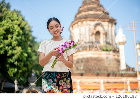 A charming Asian woman in a traditional dress stands outdoors with a pagoda in the background. A charming Asian woman in a traditional dress stands outdoors with a pagoda in the background. 120196188
