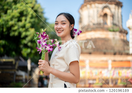 A charming Asian woman in a traditional dress smiling at the camera with a pagoda in the background. A charming Asian woman in a traditional dress smiling at the camera with a pagoda in the background. 120196189