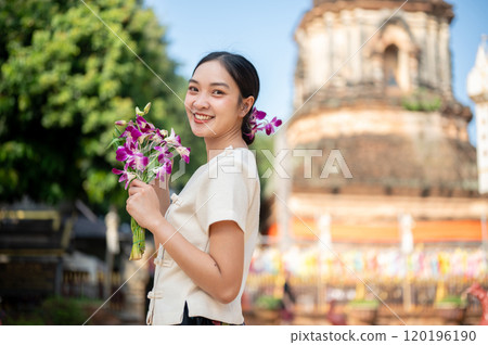 A charming Asian woman in a traditional dress smiling at the camera with a pagoda in the background. A charming Asian woman in a traditional dress smiling at the camera with a pagoda in the background. 120196190