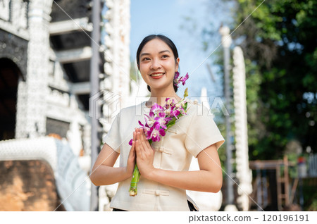 Charming Asian woman in a traditional Thai Lanna dress stands in front of a beautiful ancient temple Charming Asian woman in a traditional Thai Lanna dress stands in front of a beautiful ancient temple 120196191