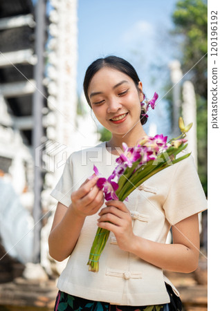 A charming Asian woman in a traditional Lanna dress admires the beautiful orchid bouquet in her hand A charming Asian woman in a traditional Lanna dress admires the beautiful orchid bouquet in her hand 120196192