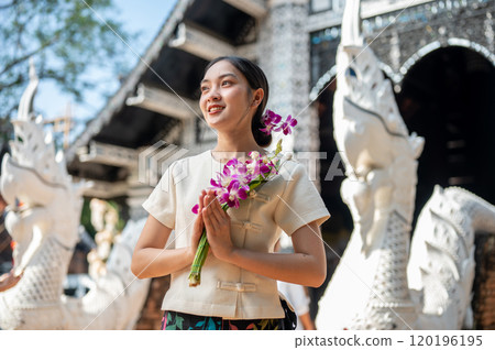 Charming Asian woman in a traditional Thai Lanna dress stands in front of a beautiful ancient temple 120196195