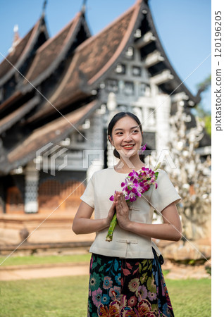 Charming Asian woman in a traditional Thai Lanna dress stands in front of a beautiful ancient temple 120196205