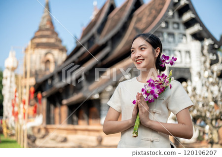 Charming Asian woman in a traditional dress stands outdoors with an ancient temple in the background Charming Asian woman in a traditional dress stands outdoors with an ancient temple in the background 120196207