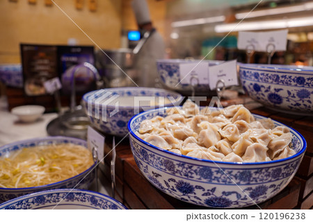 A vibrant display of traditional Chinese dumplings in a blue and white porcelain bowl, set in a bustling Shanghai market with steaming dishes nearby. 120196238