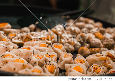 A close up view of dumplings on a pan in Shanghai, featuring translucent wrappers with orange filling and black sesame seeds, highlighting traditional cuisine. 120196267