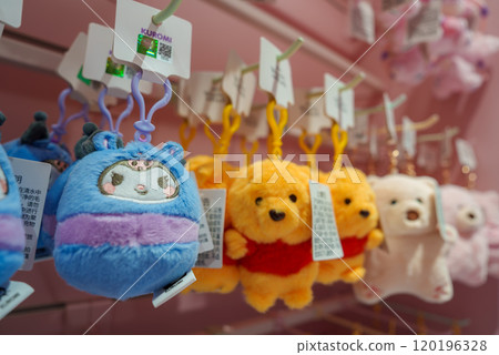 A variety of plush keychains featuring cartoon characters are displayed in a Shanghai store. Blue and purple plushies and yellow bears in red shirts are prominent. A variety of plush keychains featuring cartoon characters are displayed in a Shanghai store. Blue and purple plushies and yellow bears in red shirts are prominent. 120196328